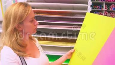 五颜六色的艺术品在一个文具店里出售。 女人在商店里选择一张彩色纸。